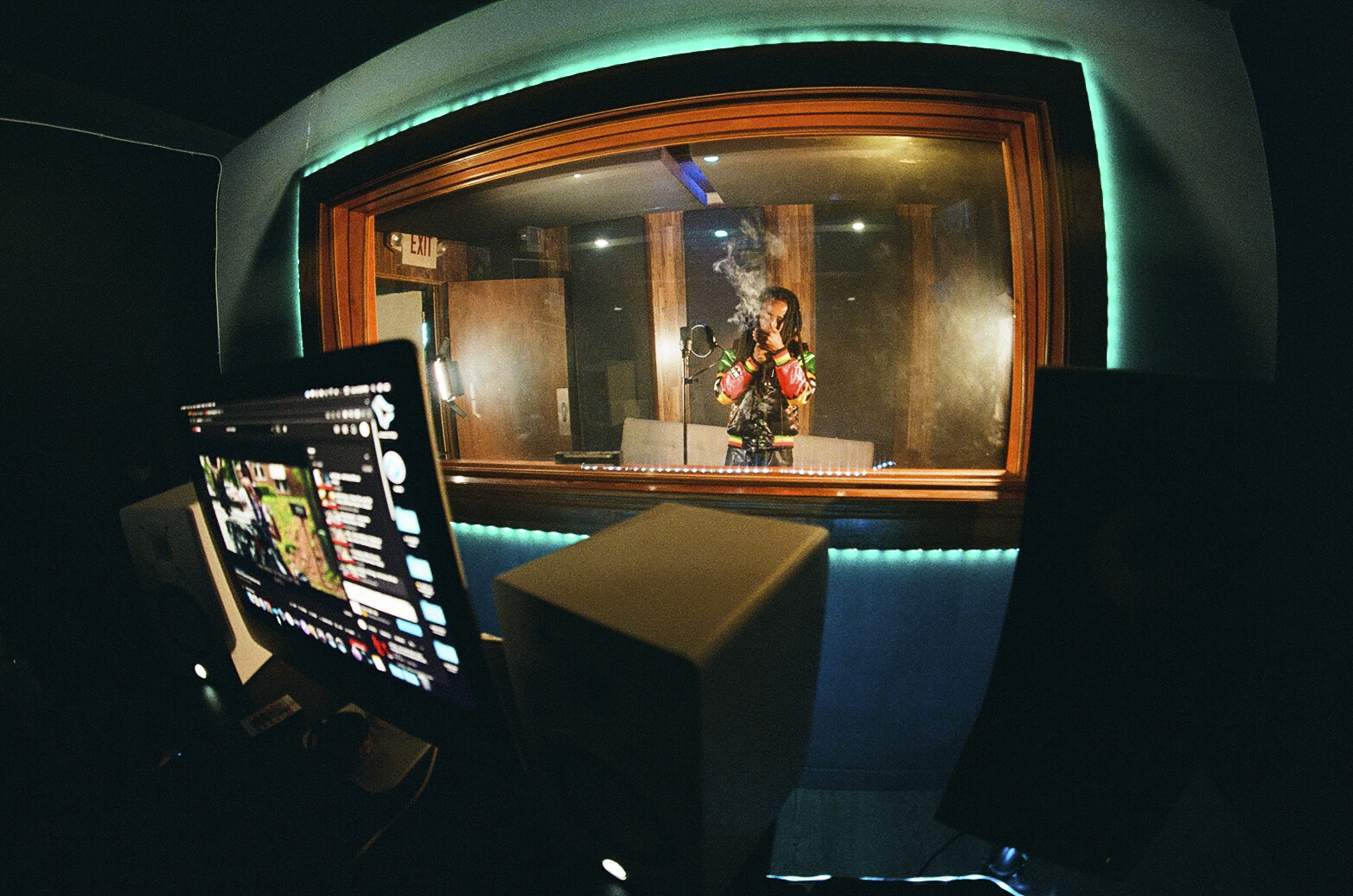 KJ Skippa Mak Marley recording in the vocal booth, seen through the studio control-room glass